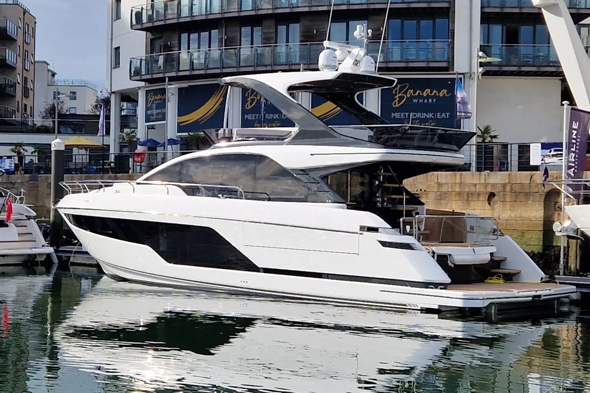 Luxury white yacht docked at Banana Wharf, with reflections on the water and nearby buildings visible.